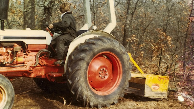 A young Wayne Harris rides a tractor in his parents' rental yard.