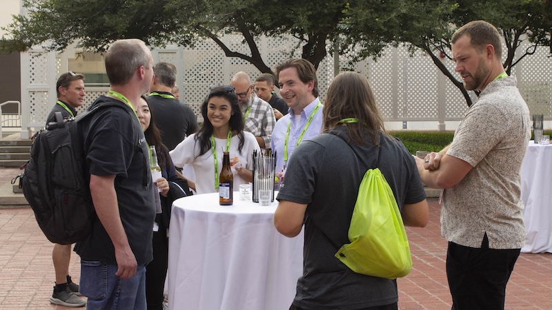 Several people stand around a cocktail table, conversing. 