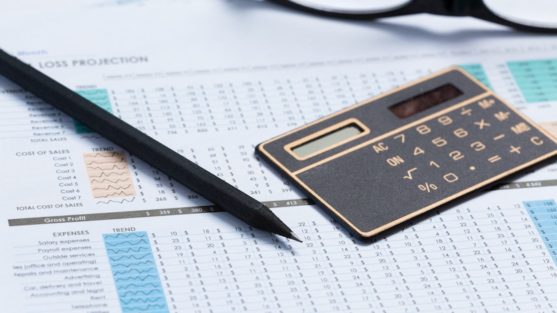 A picture of a calculator and a pen on top of some financial graphs and spreadsheets.