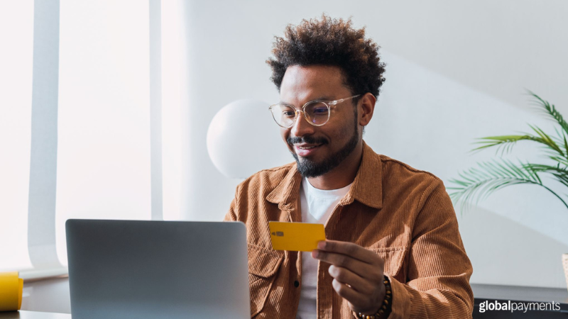 A credit card user smiles as he holds his card up while using a laptop to make a payment.