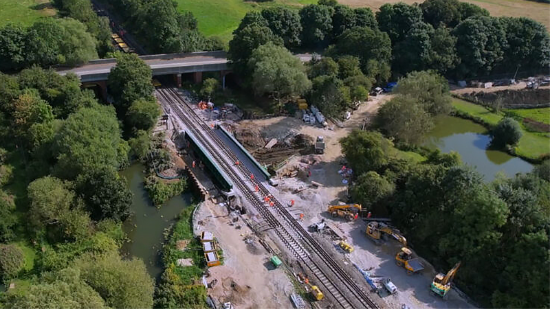 A drone photo of a rail yard within a forest with Story plant equipment around it and workers working on the rails.