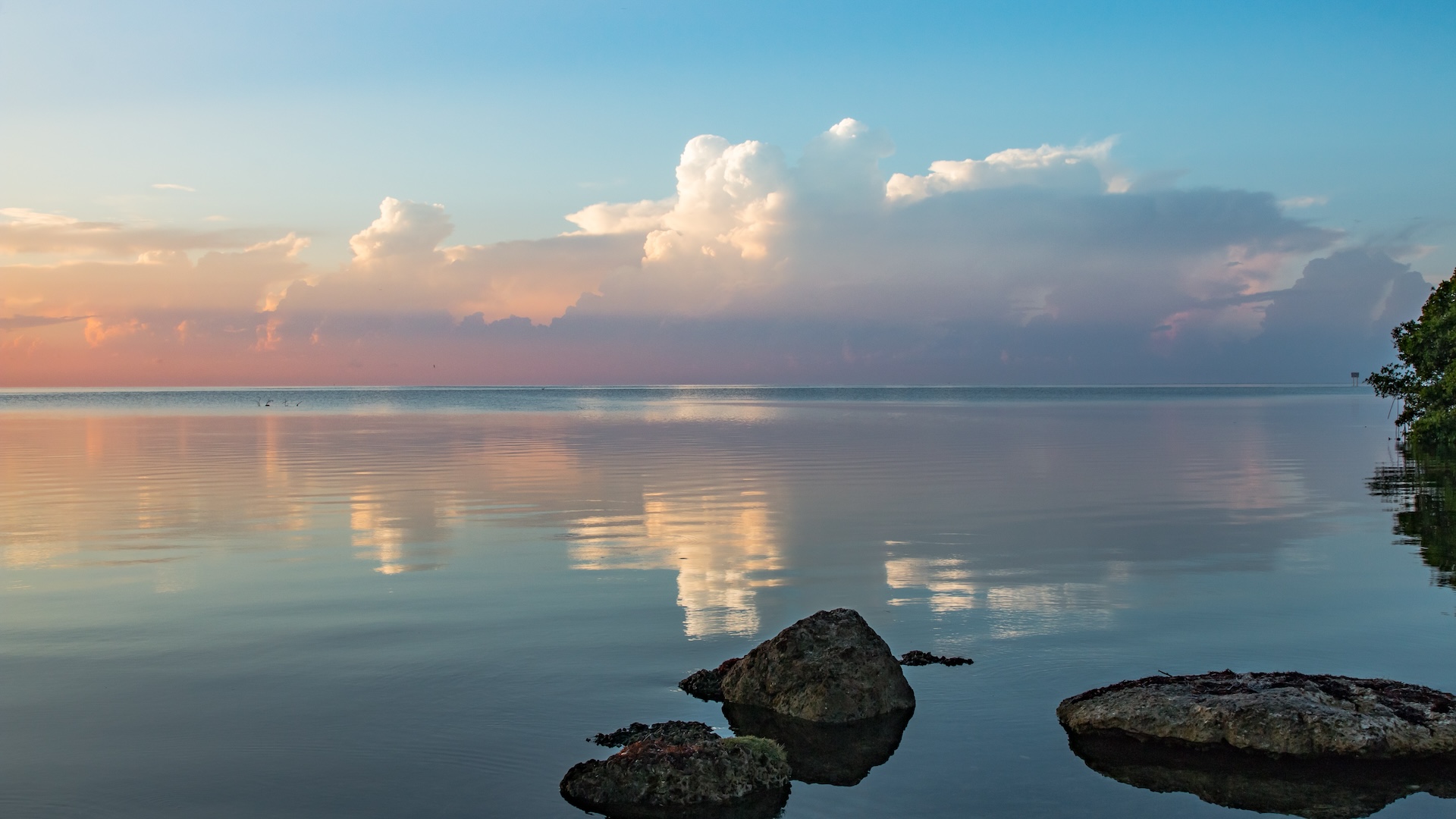 An early morning sunrise over a calm bay with a handful of large rocks in the foreground.