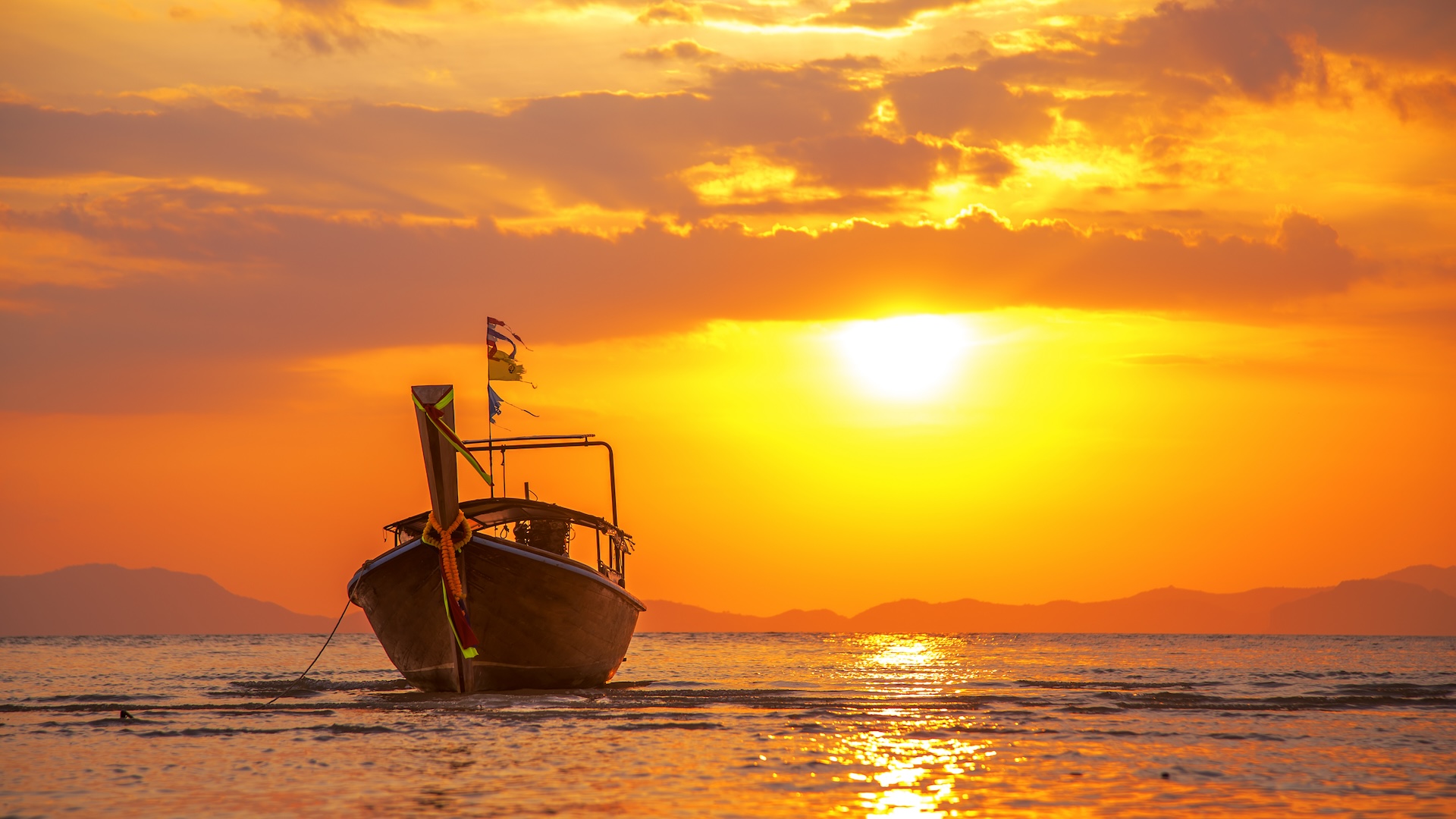 A boat on the water heading toward camera with an orange sunset in the background and calm seas.